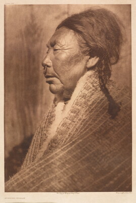 A sepia-toned photograph of an older Indigenous woman in profile with her hair in a braid, a ring through the septum of her nose, and a shawl around her shoulders.