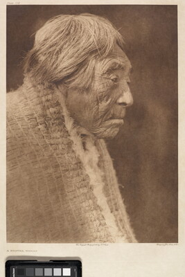 A sepia-toned portrait photograph of an elderly Indigenous woman, in profile, with short hair wearing a shawl around her shoulders.