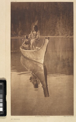 A sepia-toned photograph of two Indigenous people in a canoe floating on water.