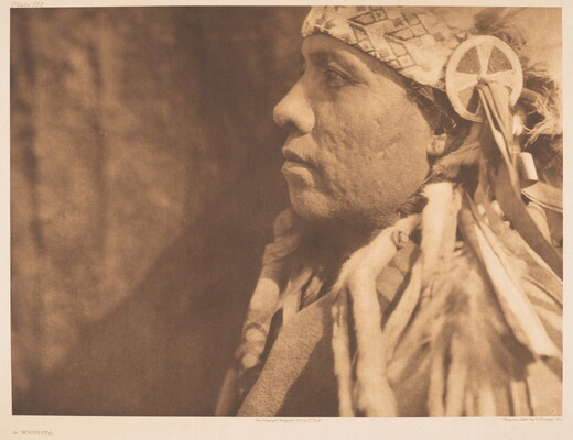 A sepia-toned, close-up, photograph of an Indigenous man in profile wearing a traditional headdress.