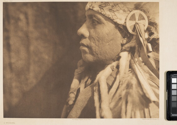 A sepia-toned, close-up, photograph of an Indigenous man in profile wearing a traditional headdress.
