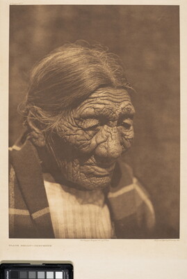 A sepia-toned photograph of an elderly Indigenous person with hair pulled back and a blanket around their shoulders.