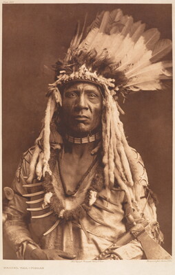 A sepia-toned portrait photograph of an Indigenous man wearing a feathered headdress with animal pelts hanging from the sides, and a bear claw necklace over a tunic.