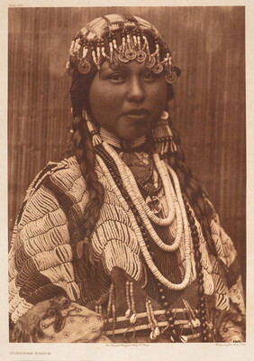 A sepia-toned portrait photograph of an Indigenous woman wearing a beaded hair covering over her braids, beaded necklaces, and an elaborately beaded tunic.