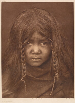 A sepia-toned portrait photograph of an Indigenous child, two braids frame their face and the rest of the hair is loose; a blanket or shawl wraps close around their chin and shoulders.