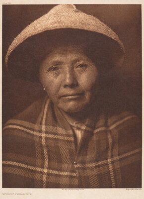 A sepia-toned portrait photograph of an Indigenous woman wearing a conical hat and a plaid blanket around her shoulders.