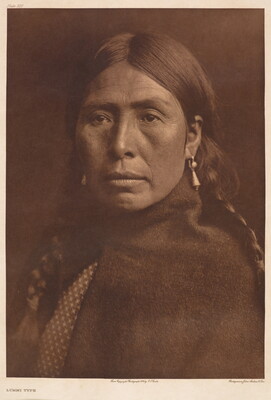 A sepia-toned portrait photograph of an Indigenous woman wearing her dark hair in braids, earrings, and a blanket or shawl around her shoulders.