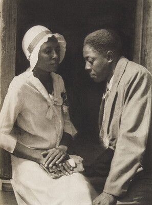 A black-and-white photograph of a young Black couple dressed nicely and seated in a doorway.
