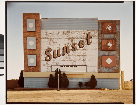 A color photograph of a weathered marquee sign for a drive-in movie theater with the word "Sunset" in script.