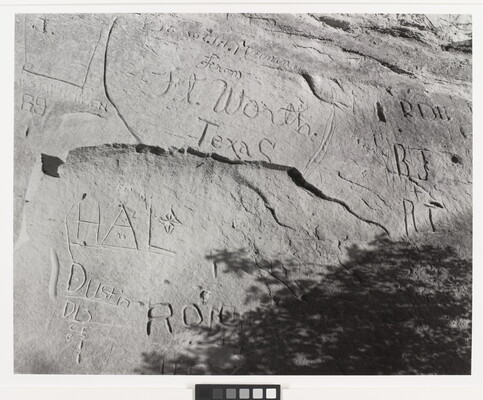 A black-and-white, tightly focused photograph of a large rock with carved inscriptions, including various initials and the words "Ft. Worth, Texas."