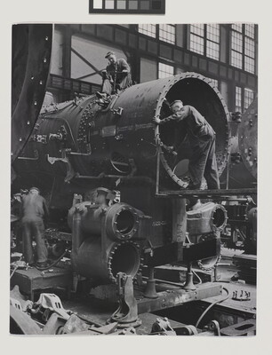 A black-and-white photograph of a few men building a locomotive car.