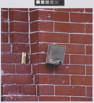 A color photograph of a doorbell and an intercom on a red brick wall.