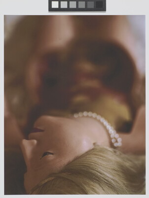 A color photograph of a White female wax mannequin with blonde hair and pearls laying down with head at the bottom of the image.