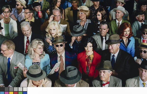 A color photograph of a crowd of people seated as if in a theater, most wearing brightly colored clothing and accessories.