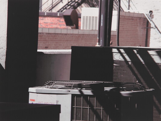 A color photograph of a large rooftop air-conditioning unit concealed by shadows in the foreground.