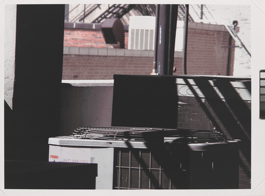 A color photograph of a large rooftop air-conditioning unit concealed by shadows in the foreground.