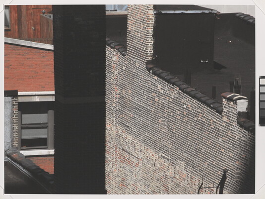 A color photograph of brick city building sides and rooftops as seen from another building window.