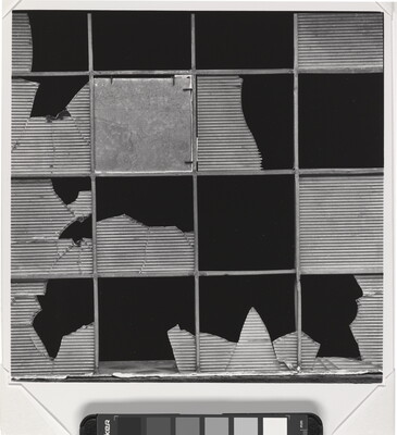A black-and-white photograph of a metal grid with broken or missing textured glass pieces in each section.