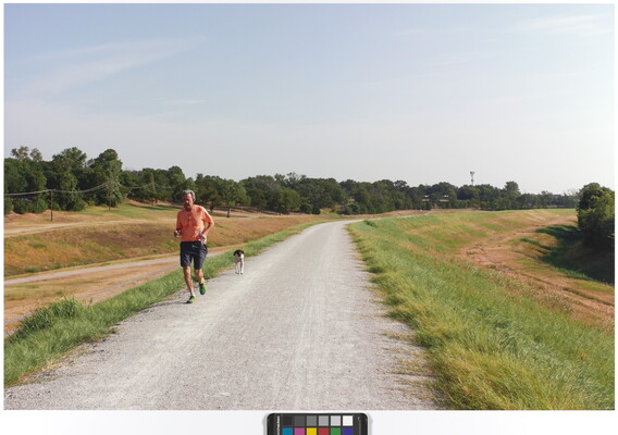A color photograph of a middle-aged White man and an unleashed dog running toward the viewer on a paved path.