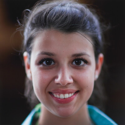 A color photograph of the face of a young, smiling White woman with dark hair pulled back from her face.