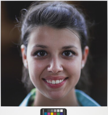 A color photograph of the face of a young, smiling White woman with dark hair pulled back from her face.