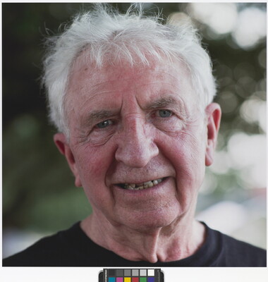 A color photograph of the head and shoulders of a smiling older White man with white tousled hair.