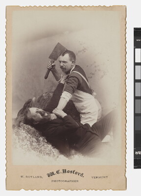 A sepia-toned studio photograph of a White man in a butcher's apron holding a cleaver with one hand as he holds by the neck another White man who is reaching up toward the cleaver.