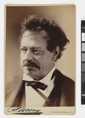A sepia-toned studio portrait photograph of a middle-aged White man with unkempt hair, a mustache, wearing a black jacket, white shirt with a high collar, and bow tie.
