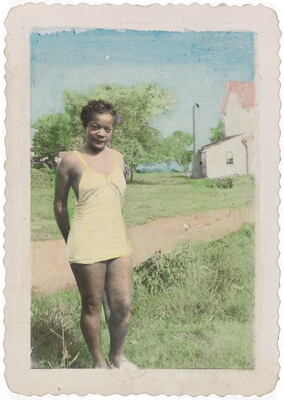 A color photograph of a young Black woman wearing a yellow one-piece bathing suit standing in grass beside a dirt road.