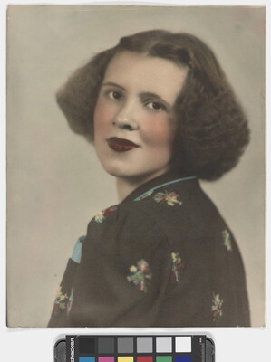 A color portrait photograph of a White woman with curly bobbed hair, wearing a floral top looking over her shoulder at the camera.