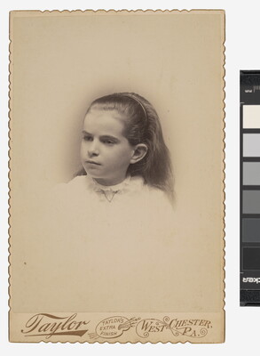 A black-and-white studio photograph of the head and shoulders of a young White girl with long hair held back in a headband.