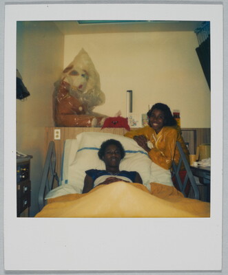 A color Polaroid photograph of two Black women, one lying in a hospital bed and the other leaning against the bed frame.