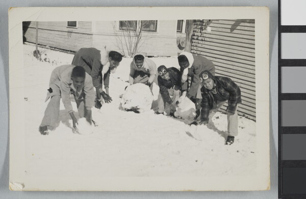 A black-and-white snapshot of smiling Black children building snowmen next to a house.