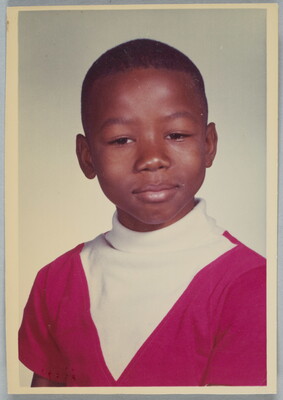 A color school photograph of a Black child with short hair wearing a white and red turtleneck.