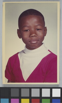 A color school photograph of a Black child with short hair wearing a white and red turtleneck.