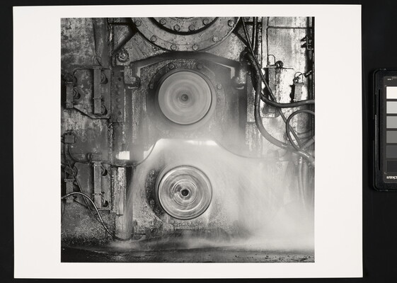 A black-and-white photograph of two spinning metal discs set into a metal wall that has pipes and tubes connected to it.