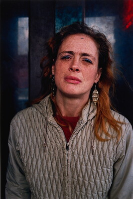 A color portrait photograph of a White woman with long hair squinting and wearing a gray quilted jacket.