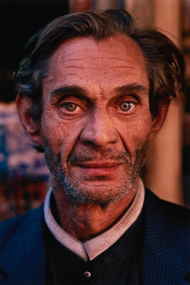 A color photograph of a middle-aged White man with large and intense hazel eyes, stubble on his face, wearing what might be a clerical collar.