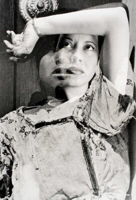 A black-and-white, double-exposure photograph of two portraits of women posed with their arm over their heads and gazing upward.