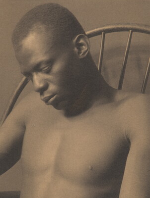 A sepia-toned photograph of a shirtless Black man napping in a chair.
