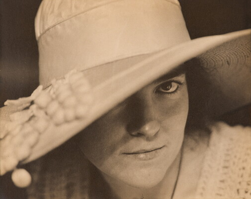 A black-and-white close-up photograph of a White woman wearing a large brimmed hat that covers one of her eyes.