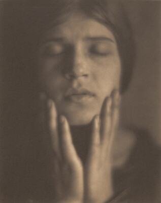 A black-and-white photograph of the face of a fair-skinned woman, eyes closed, hair pulled back, holding her hands to her face.