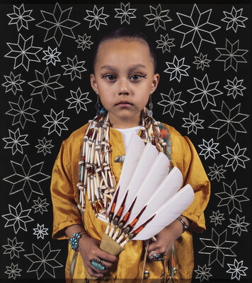 A color photograph of a young Indigenous girl, dark hair pulled back, wearing a yellow shirt, beaded necklaces, turquoise jewelry, holding a feathered fan, standing in front of a black background with white stars.
