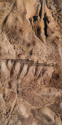 A color photograph of an aerial view of a desert with power lines that cast bar code-like shadows on the ground.