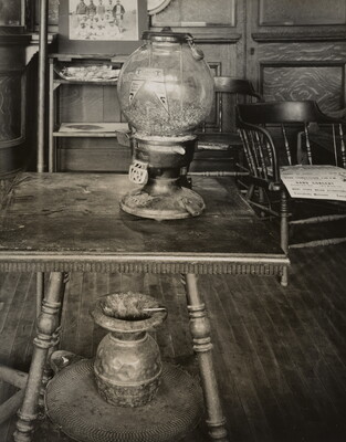 A black-and-white photograph of an old gumball machine sitting on an antique table.
