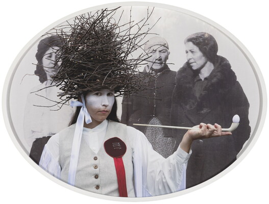 An oval color photograph of a person with their face painted white, wearing a twig hat and a white blouse and vest, holding a long thin pipe; the color photo is layered on top of a black-and-white photograph of three women.