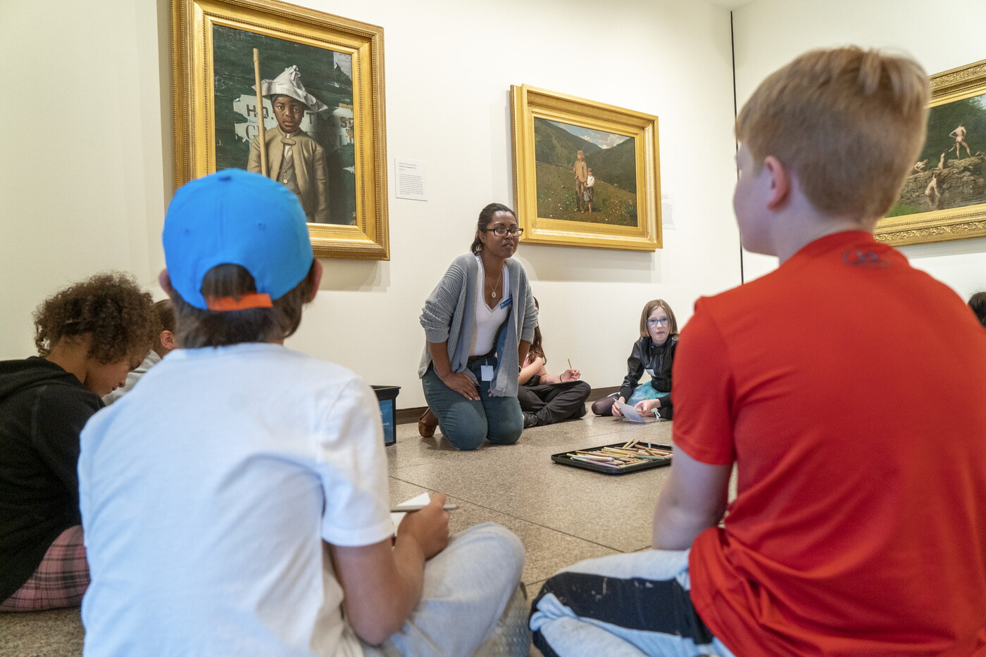 A Carter educator leads a discussion with students seated on a gallery floor around her.