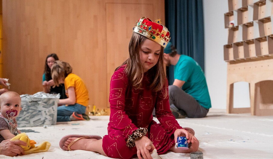 A child sits on the floor and holds art supplies in her hands.