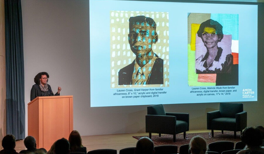 In the Carter's auditorium, a woman stands at a podium next to a screen showing artwork.