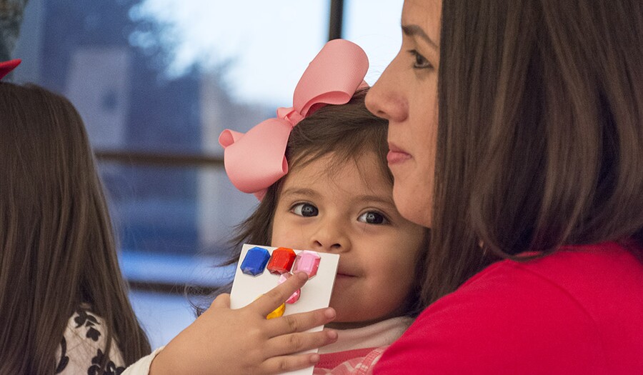 A close-up of a toddler sitting in a woman&#039;s lap.